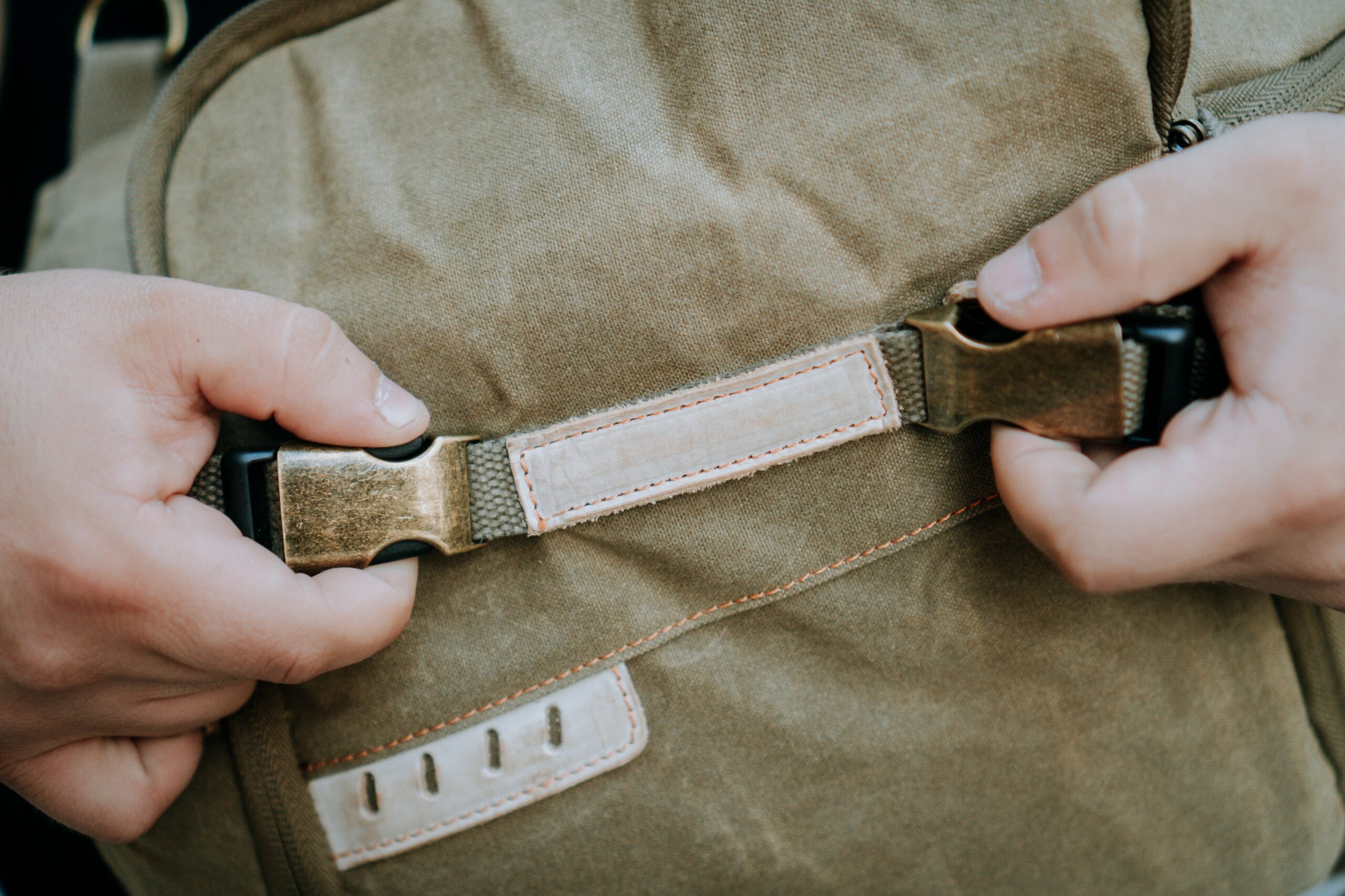 A closeup shot of buckle and strap of a brown canvas camera utility bag with recycled material